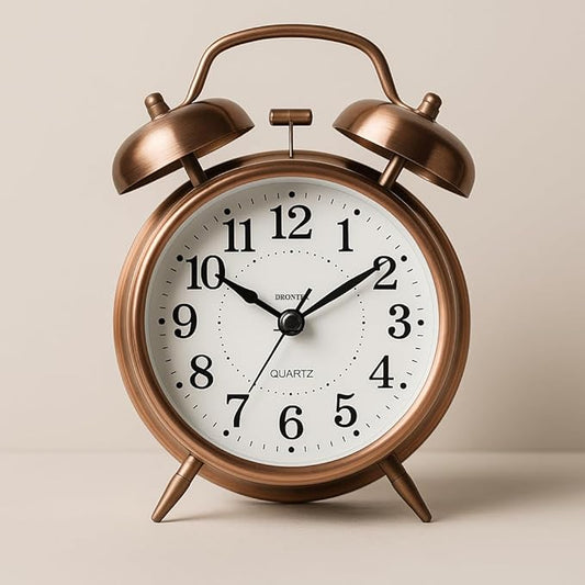 Bronze alarm clock with white face on a beige background